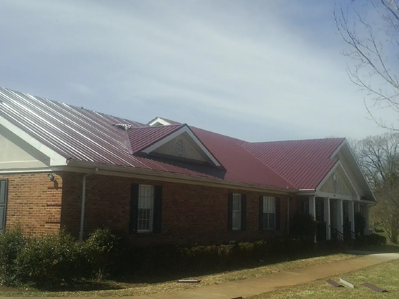 Red metal roof with gabled entries on a long brick building, from a Hail Damage Roof Repair job in Husum
