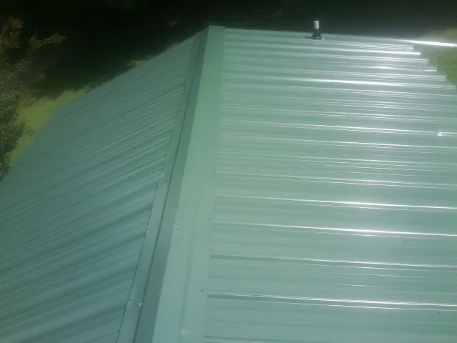 New green metal panels meeting at the ridge of a roof — Flat Roof Repair work by our crew in Husum