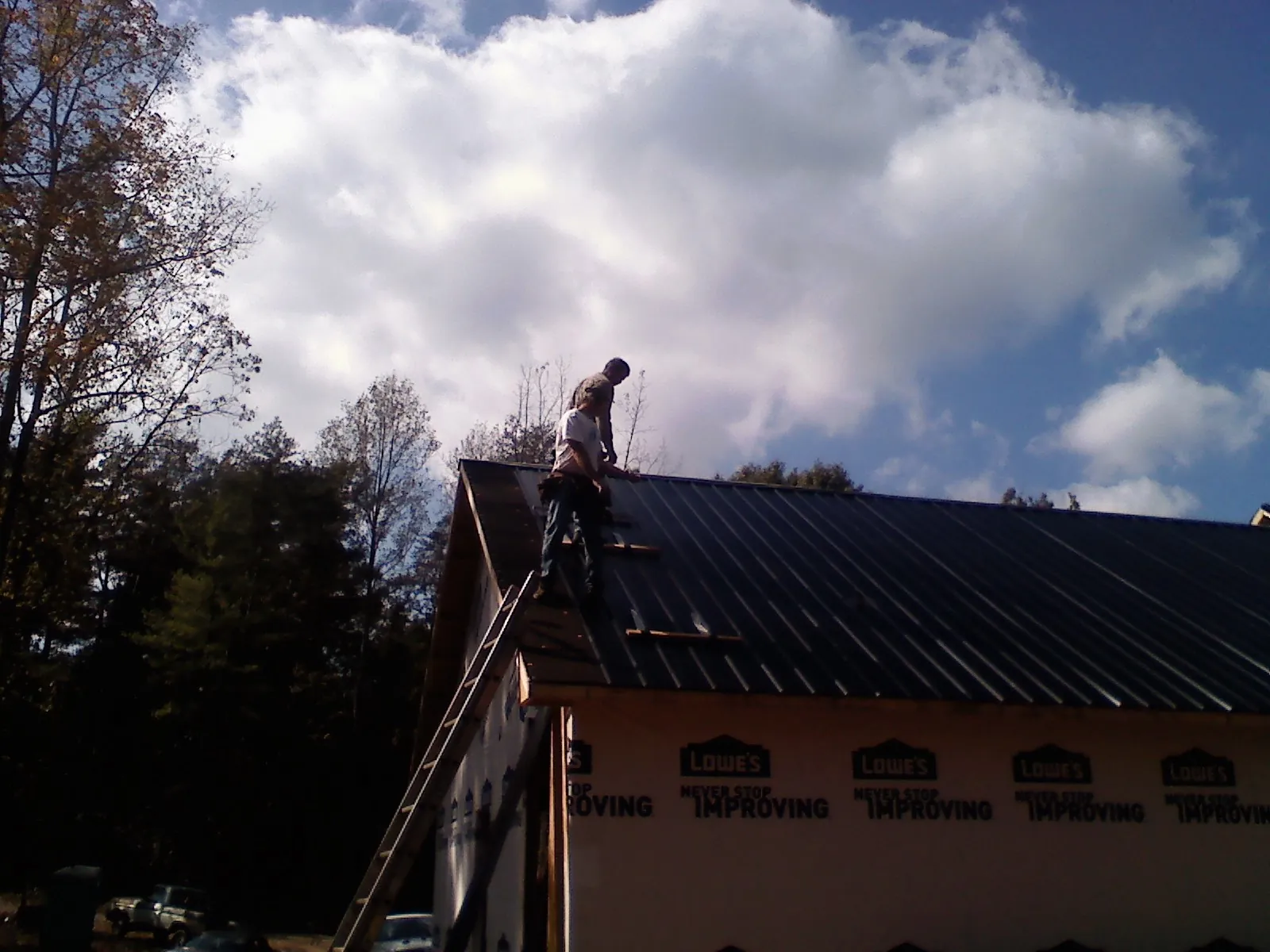 Roofer fastening dark metal panels high against a cloudy sky, from a Roof Inspection job in Husum